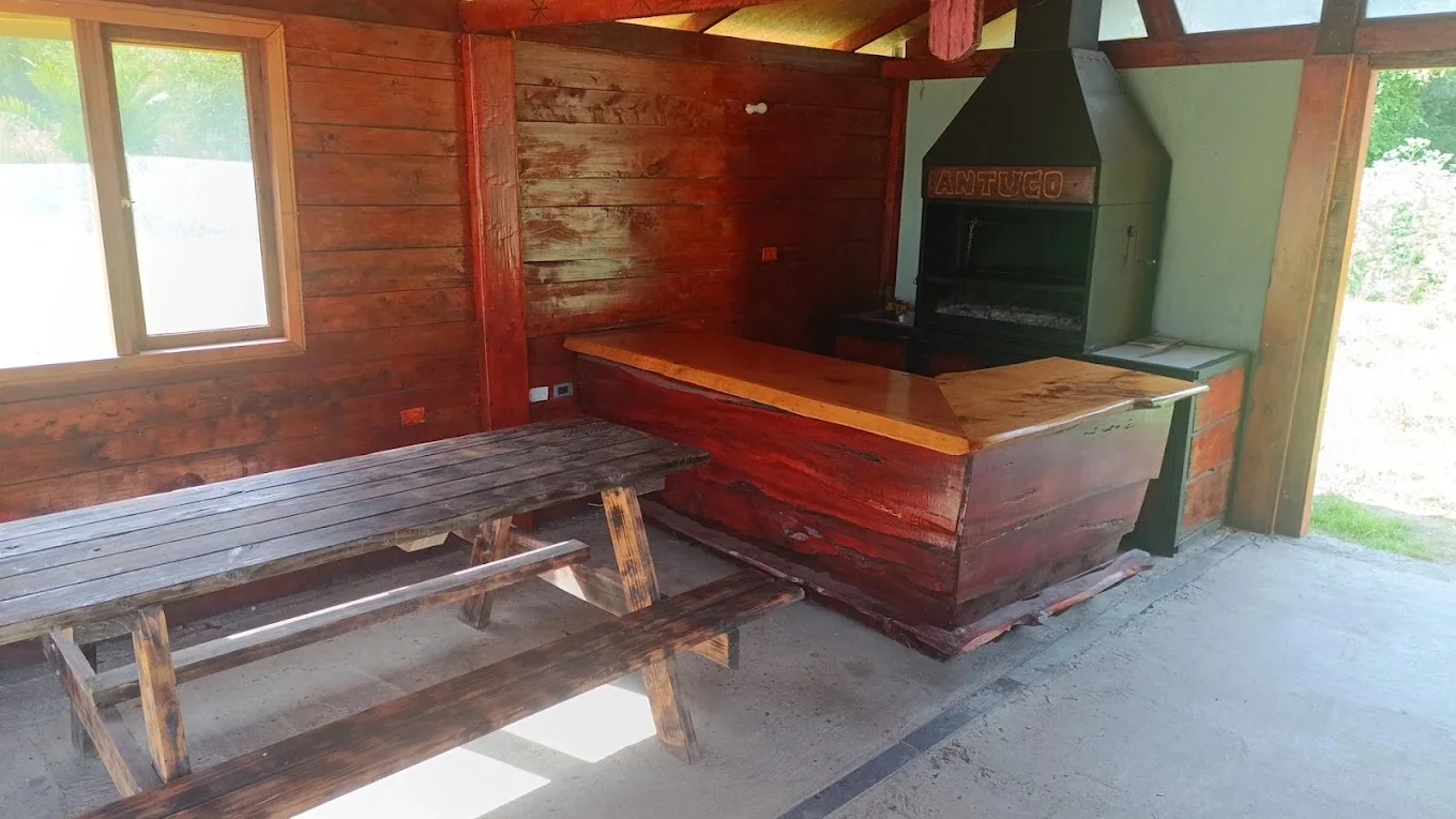 Interior de un quincho con mesa de madera, barra y parrilla